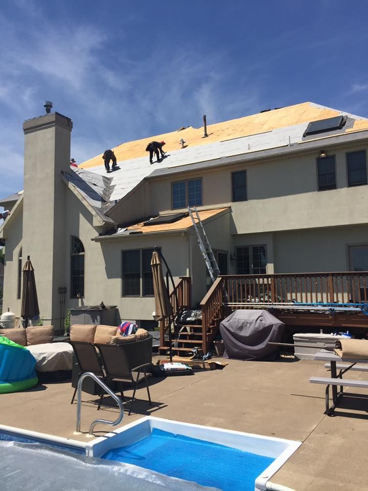 Two workers install new roof sheeting on a sunny day above a patio with a swimming pool and deck.