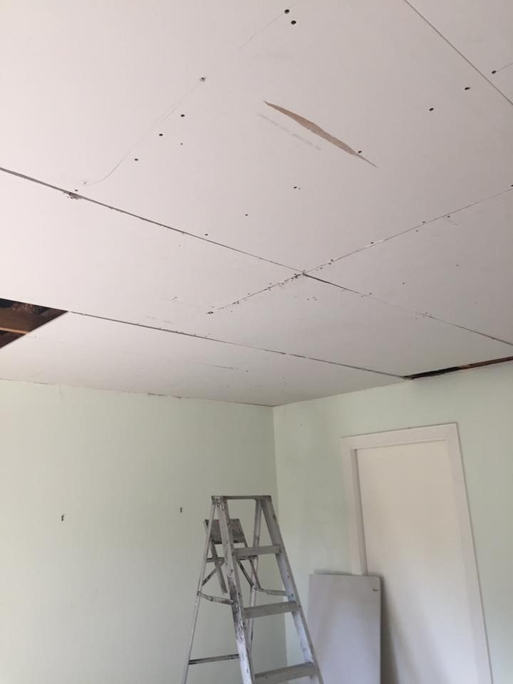 An unfinished drywall ceiling with gaps and screw marks, shown above a pale green room with a step ladder.