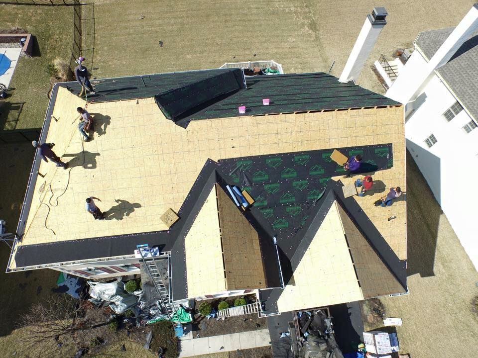 A high-angle view of workers installing new roofing shingles on a residential home with exposed wooden sheathing.