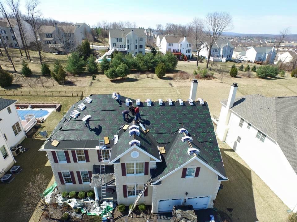 Aerial view of workers replacing shingles on a suburban house roof in a residential neighborhood.