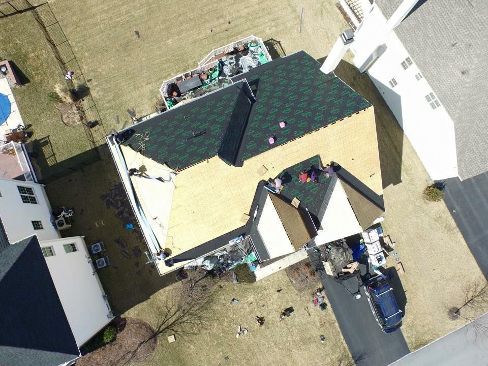 An aerial view of workers installing dark green shingles on a residential roof over bare wooden sections.