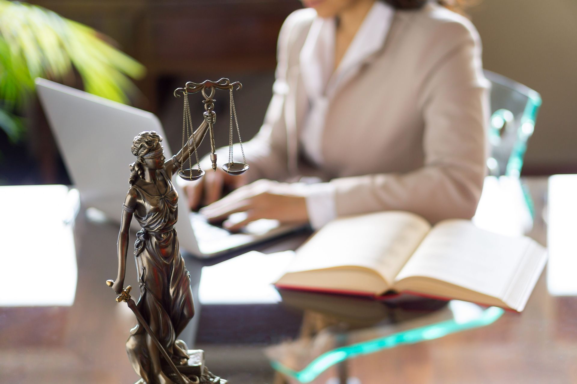 A statue of Lady Justice and a cropped view of a lawyer working on a laptop in the background.
