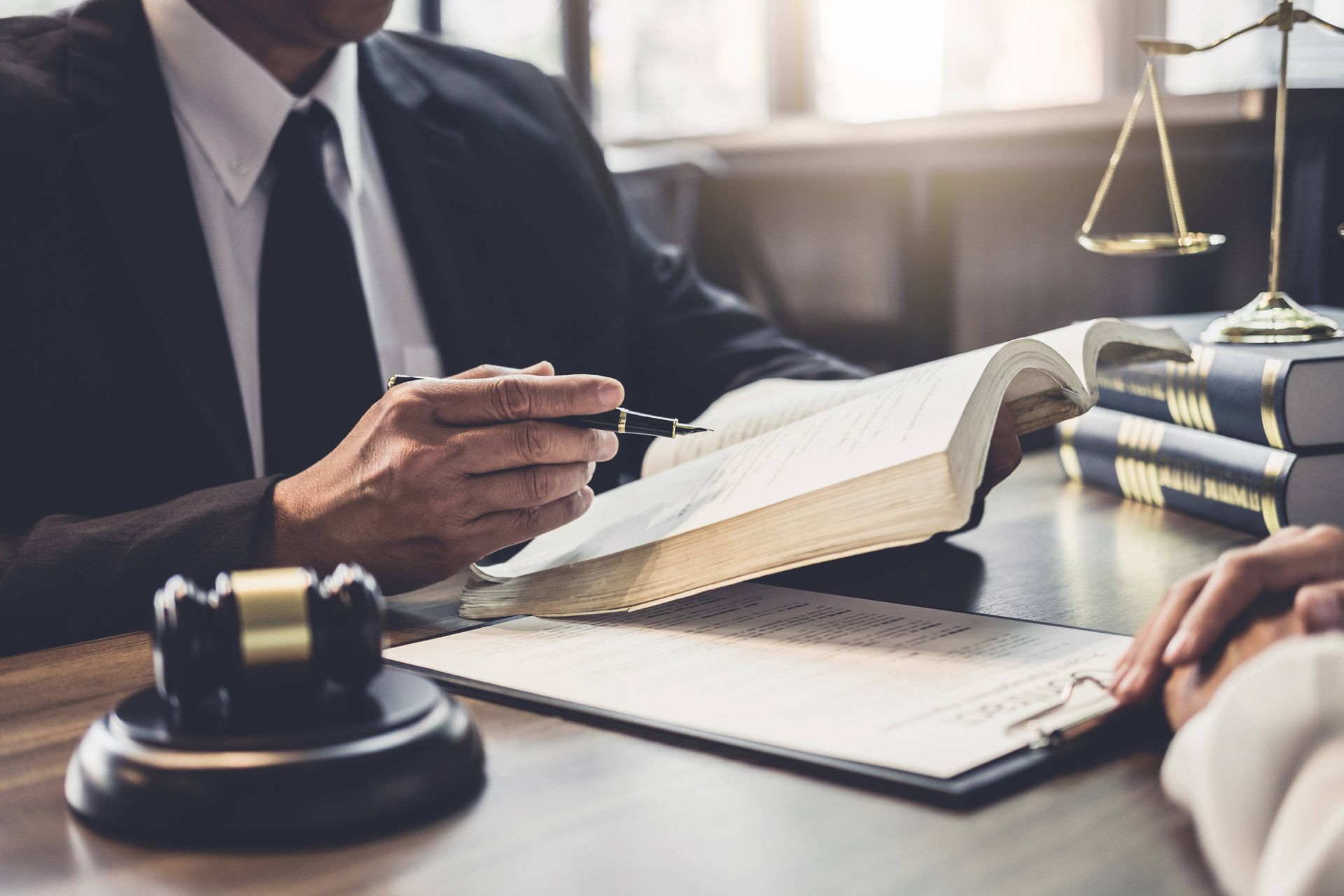 A cropped view of a lawyer consulting a book with a client in his office.