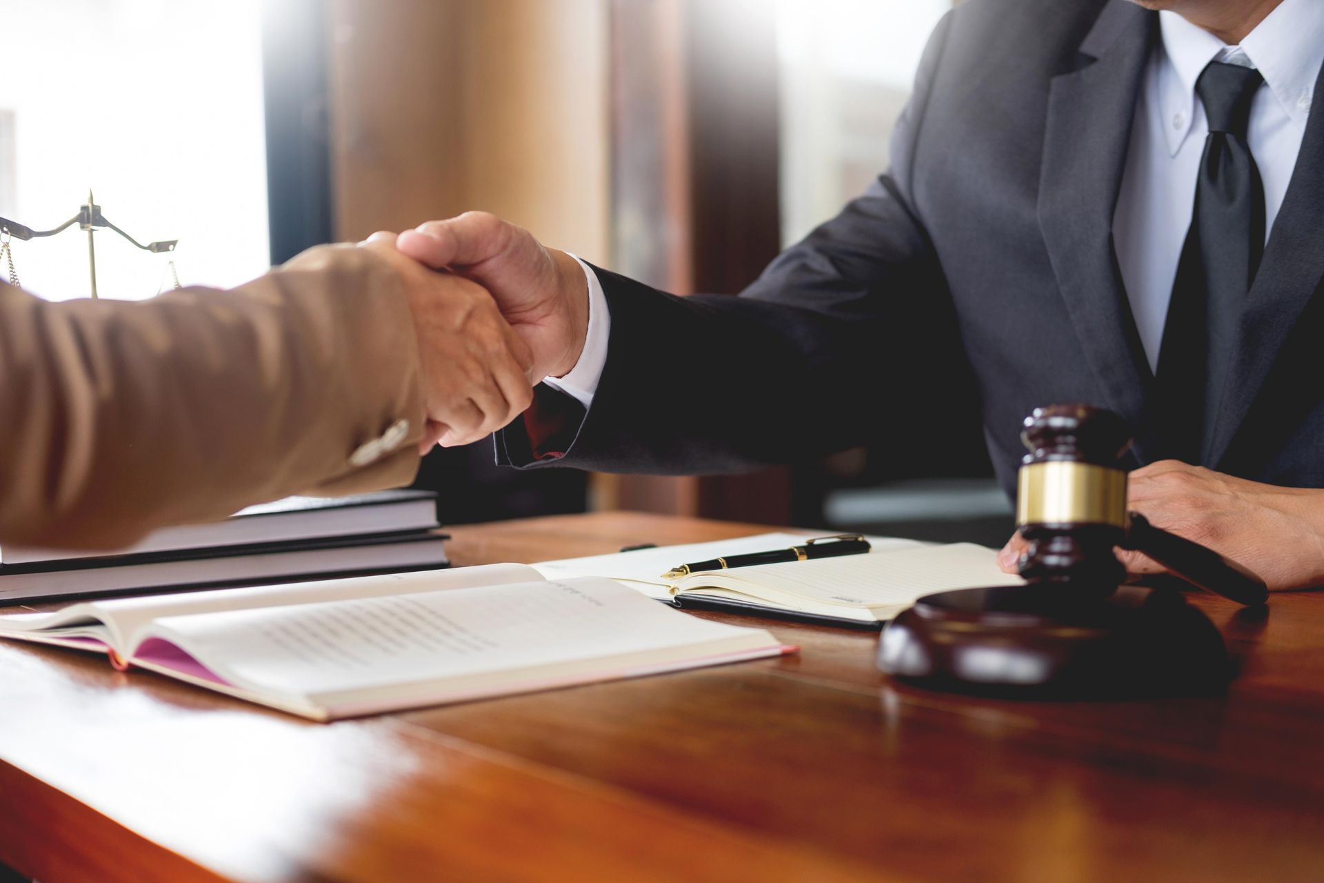 A cropped view of a lawyer shaking hands with his client over a desk with a wooden gavel.