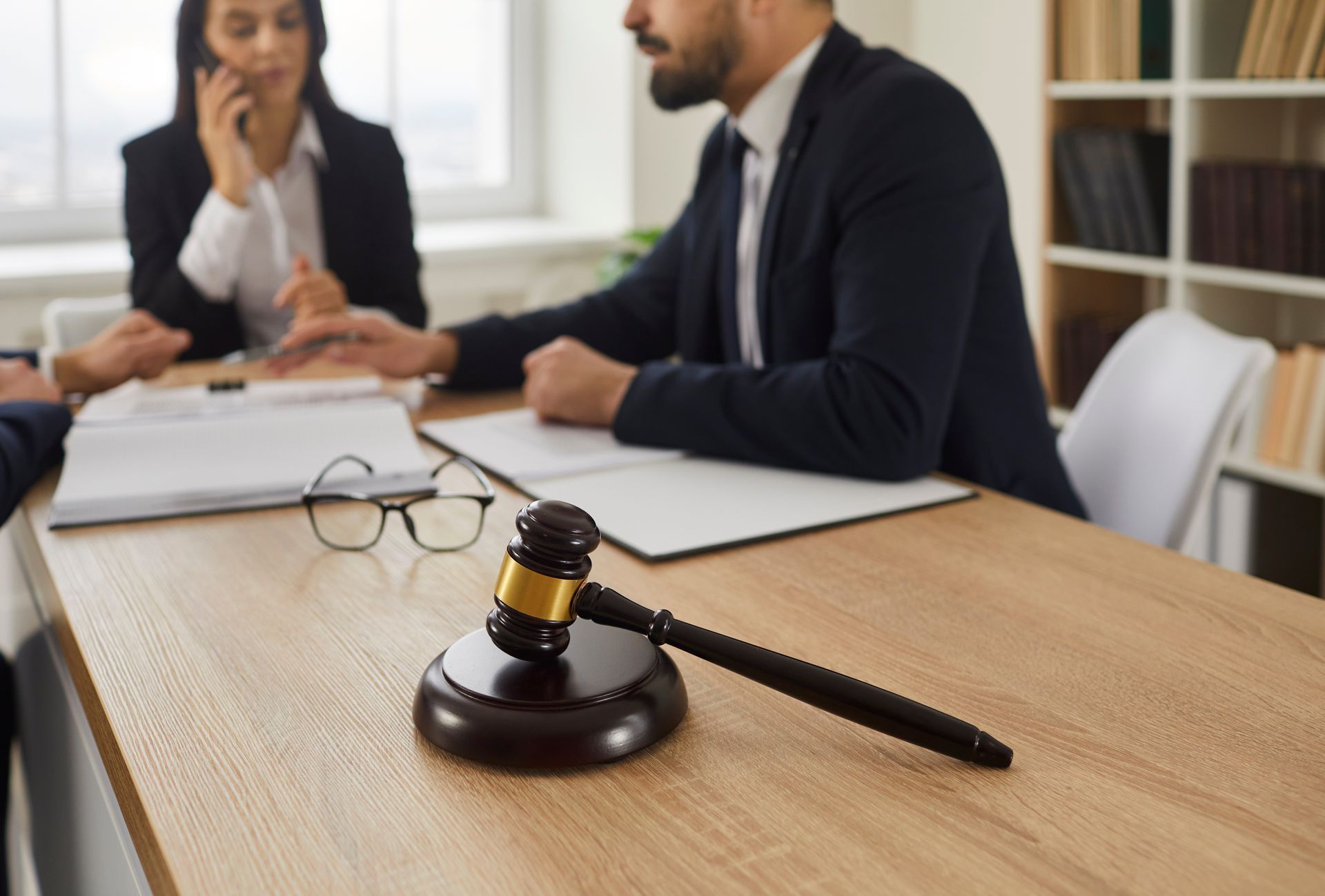 A gavel is on a table, and there is a meeting between three lawyers in the background.