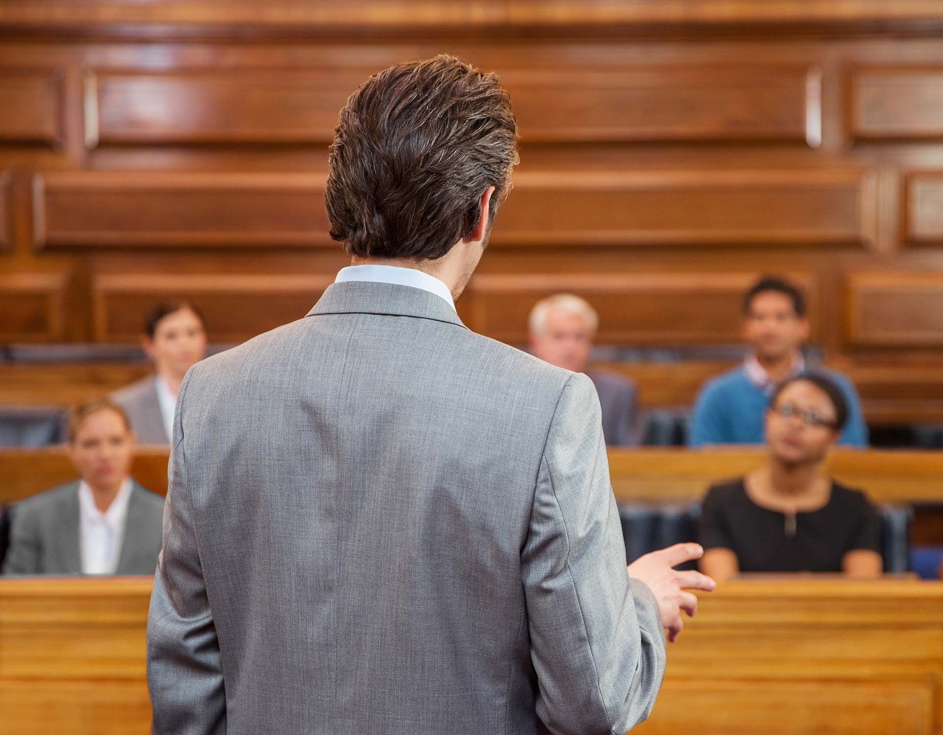 A rear view of a lawyer pleading his case to jurors in a court room.