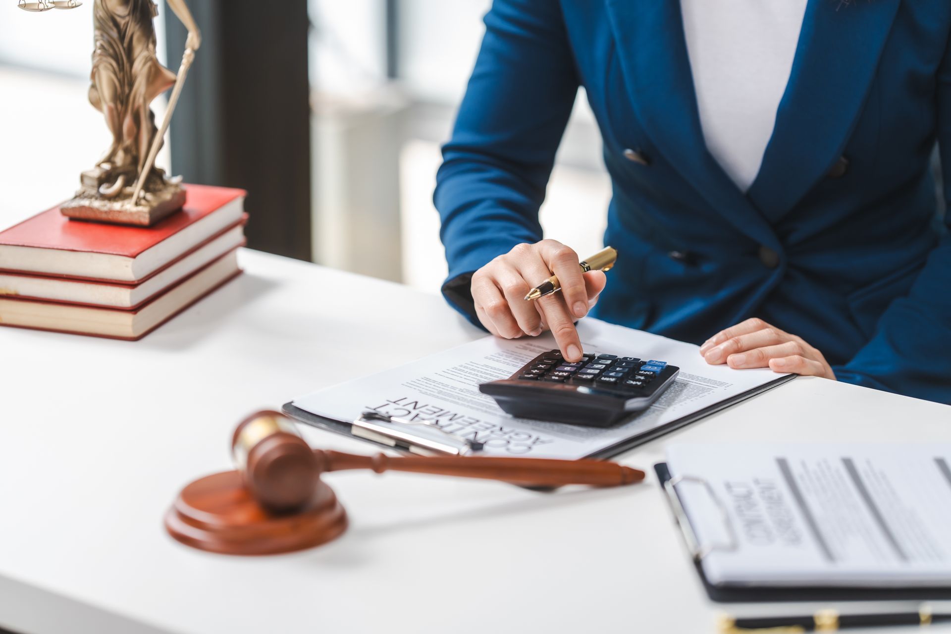 A partial view of a lawyer calculating expenses with a legal contract, gavel & law books on a table. A partial view of a lawyer calculating expenses with a legal contract, gavel & law books on a table.