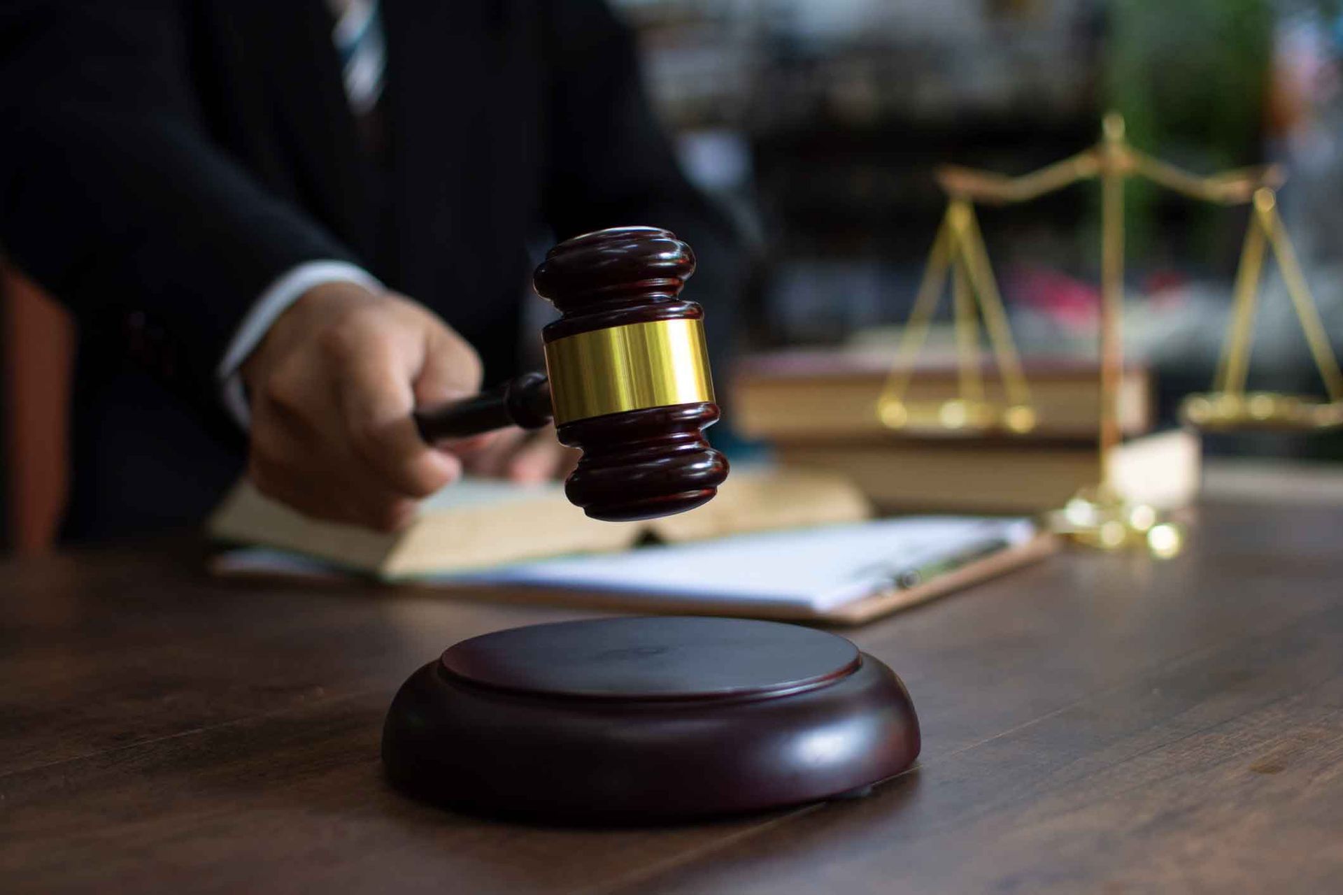 A judge is holding a wooden gavel in front of a wooden table.