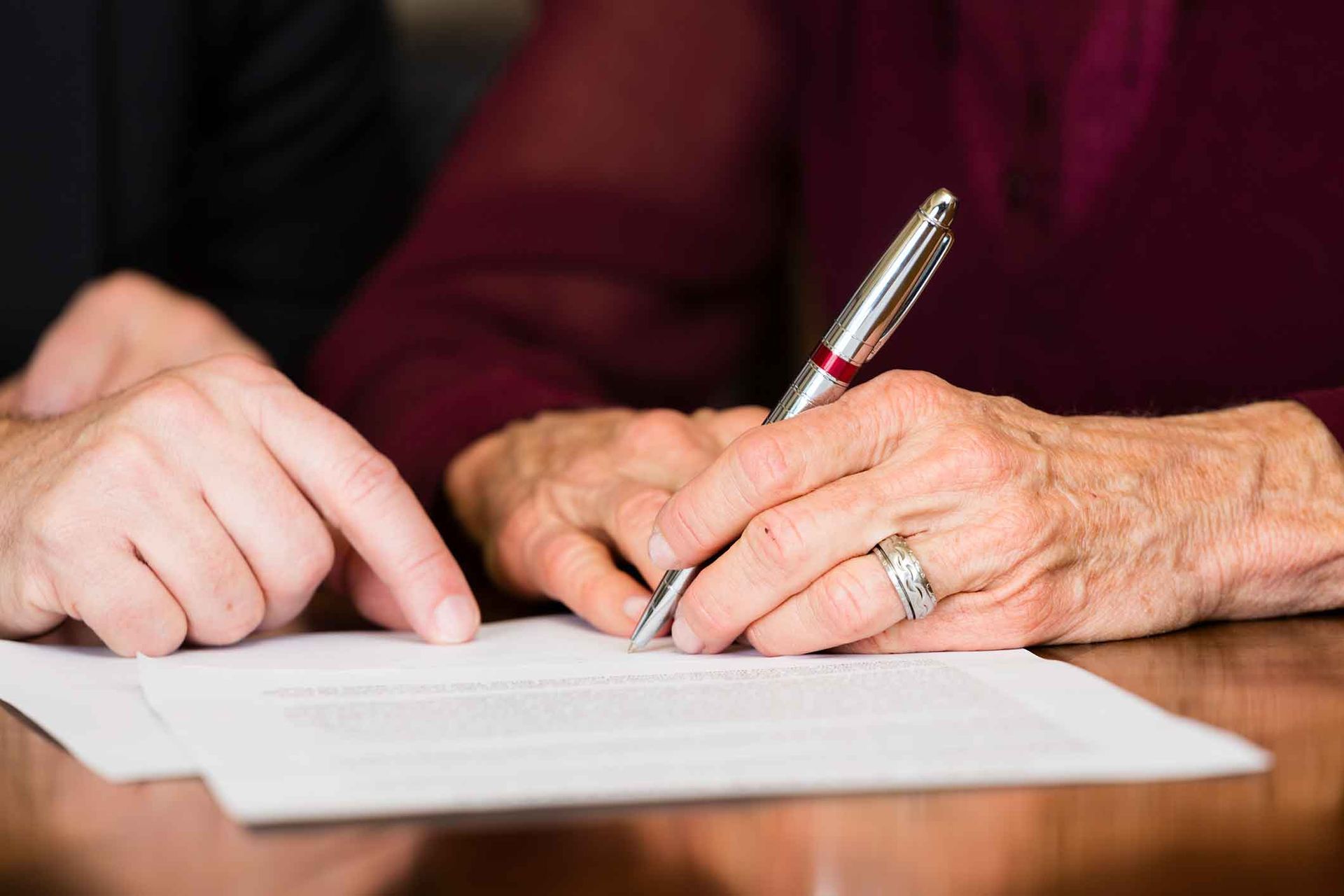 An elderly woman is signing a document with a pen.