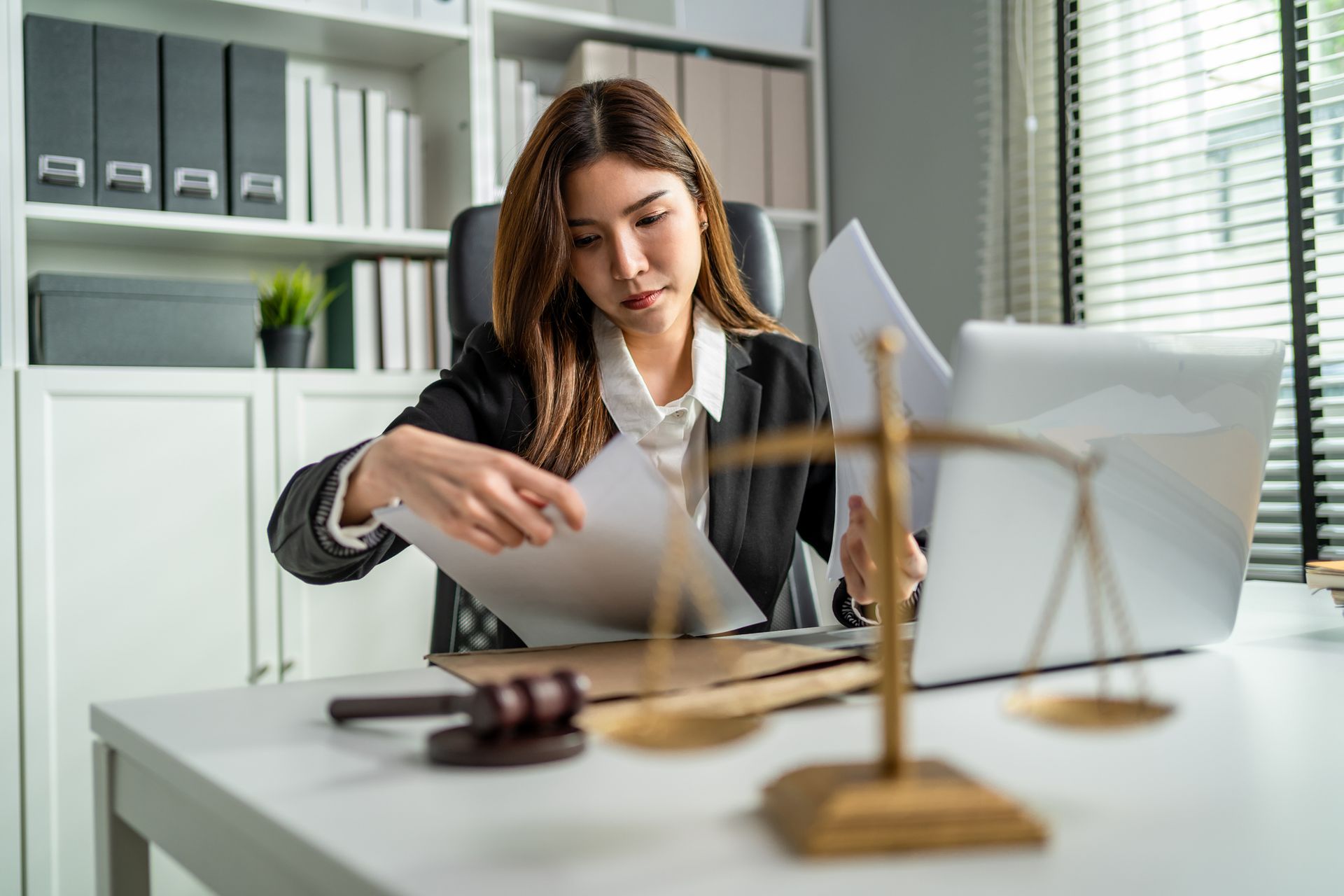 An Asian lawyer woman with a hammer and scales of justice looks at a document sitting in an office