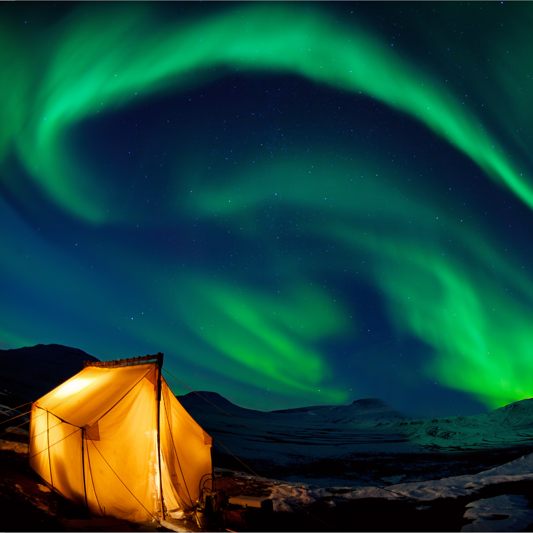 A tent is lit up under the aurora borealis