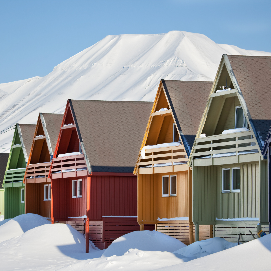 A row of colorful houses in the snow with a mountain in the background