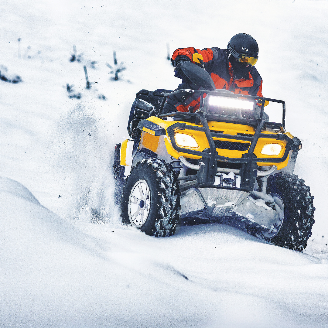A man is riding a yellow atv in the snow