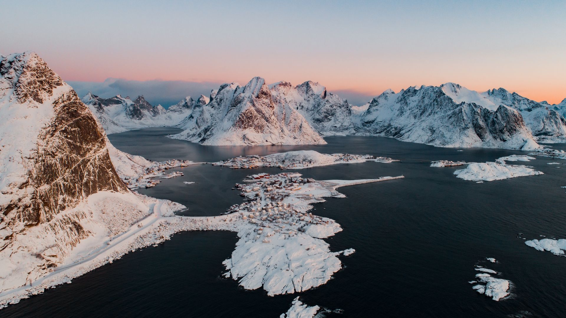 An aerial view of a lake surrounded by snow covered mountains.