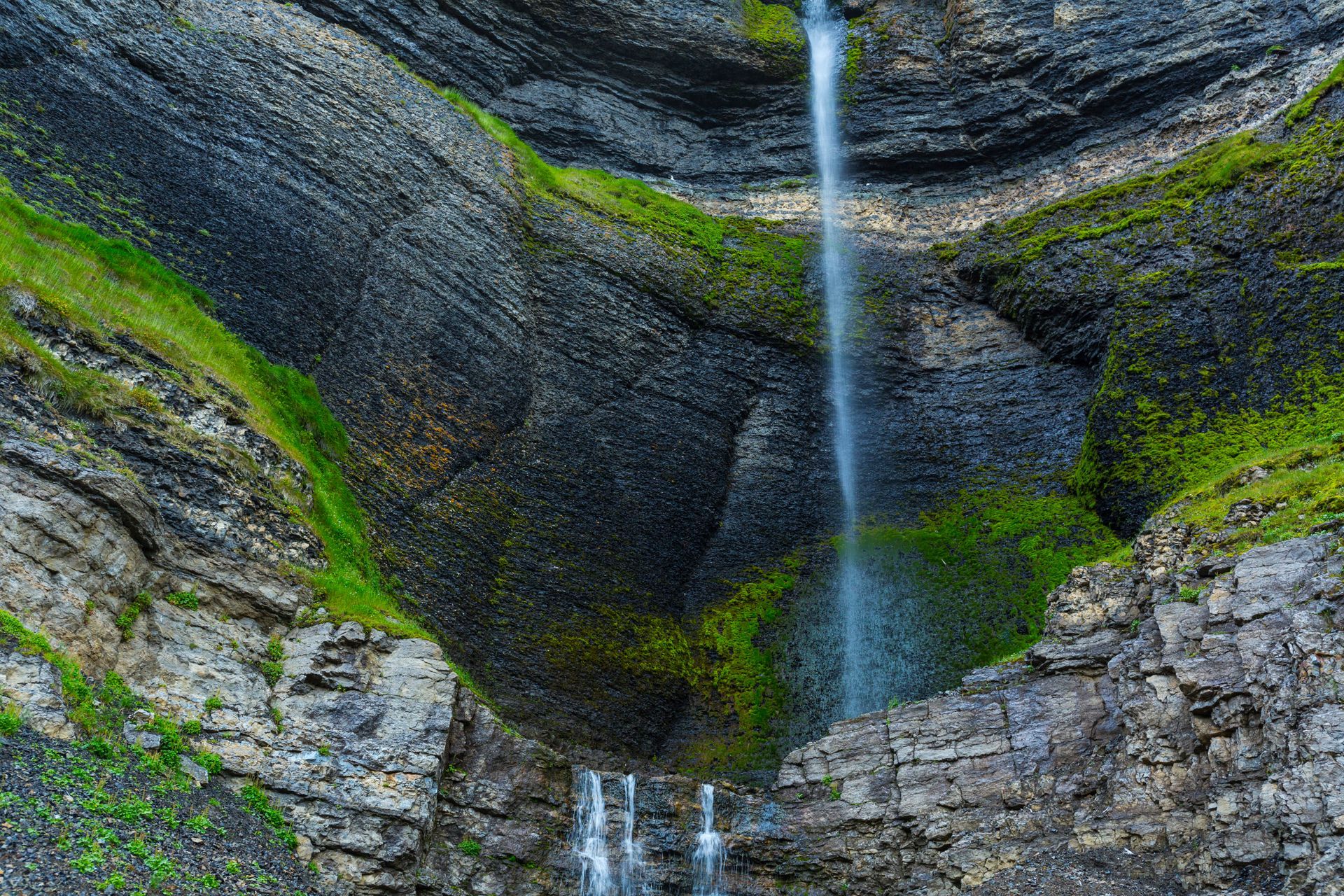 A waterfall in the middle of a canyon surrounded by rocks and grass.