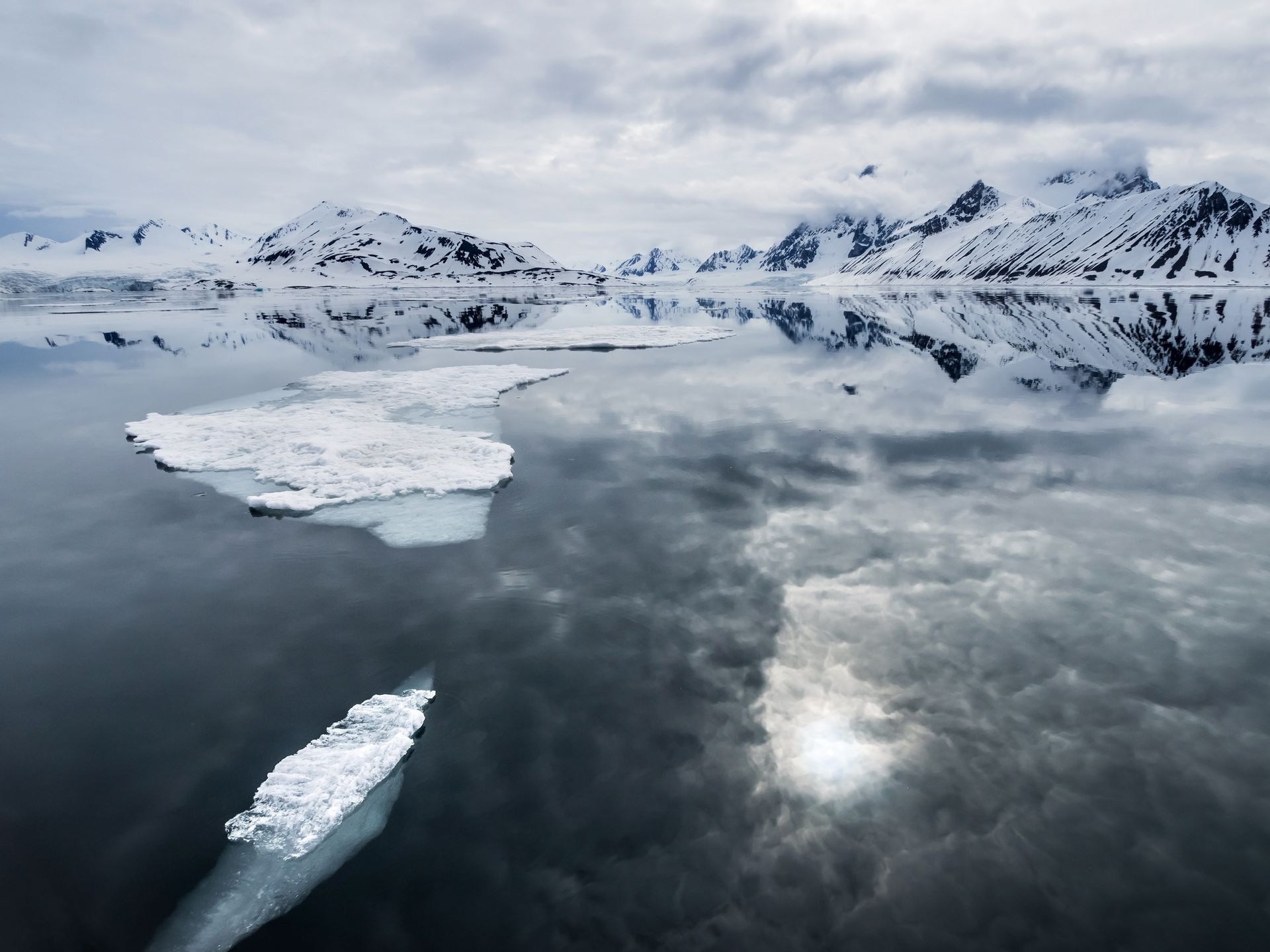 A large iceberg is floating on top of a body of water with mountains in the background.