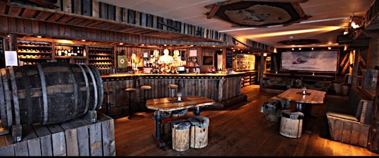 A restaurant with wooden tables , chairs , barrels and a bar.
