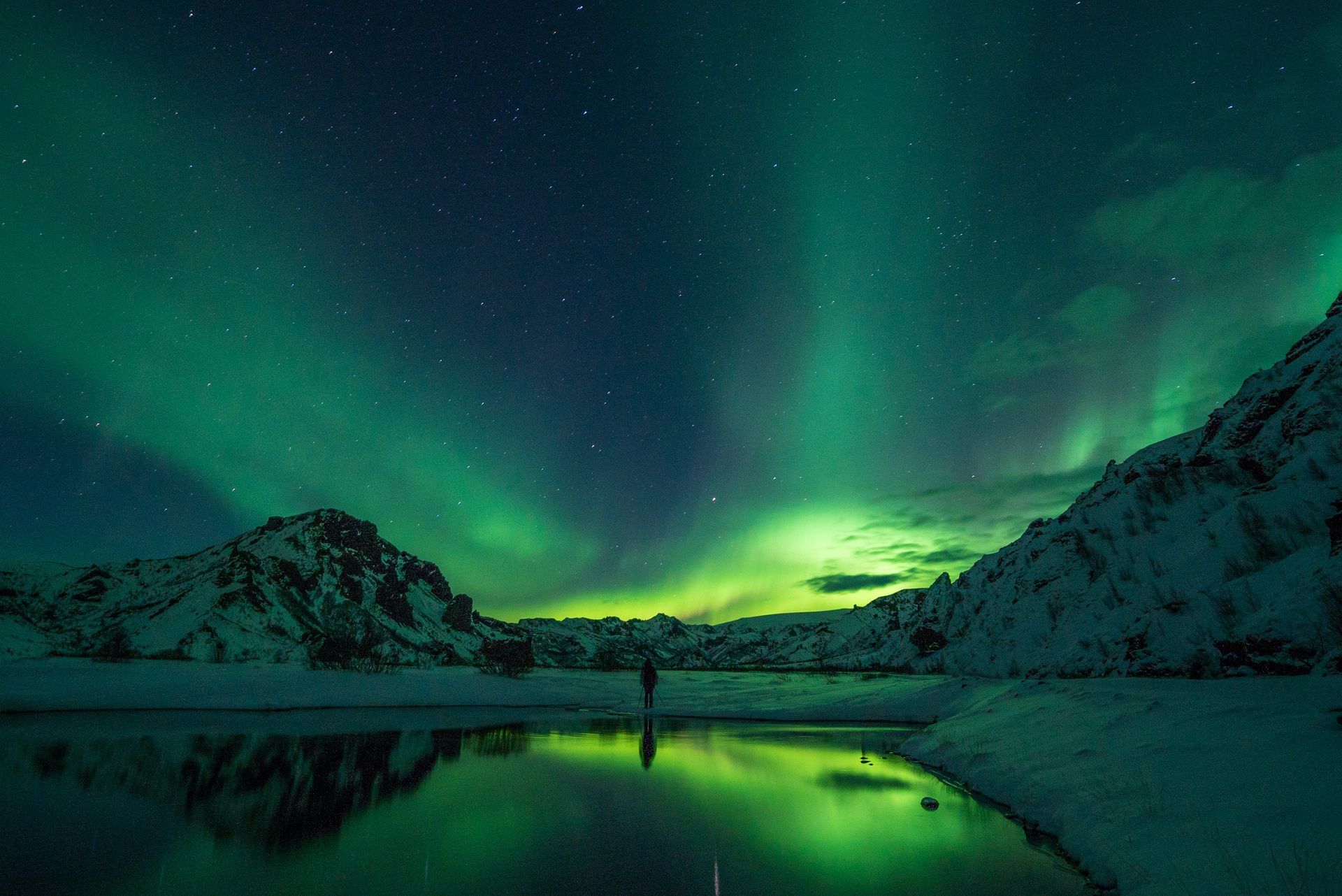 A person is standing in the water under the aurora borealis.