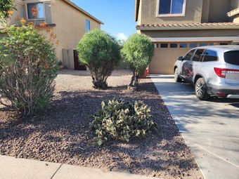 Front yard with gravel landscaping, shrubs, and a parked silver SUV beside a beige house.
