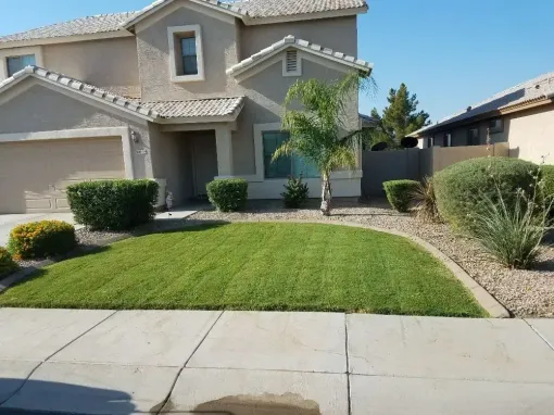 Suburban two-story house with a manicured lawn, shrubs, and a sidewalk in front