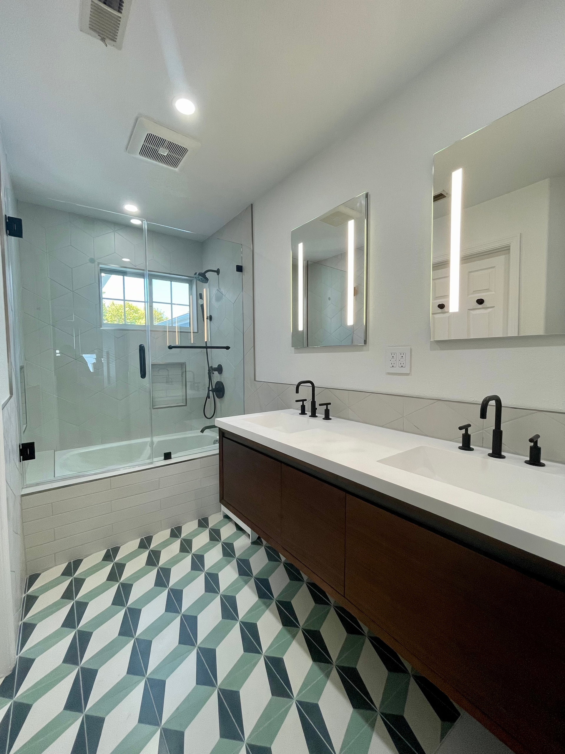 Bathroom with dark wood vanity, patterned tile floor, glass shower, and two mirrors.