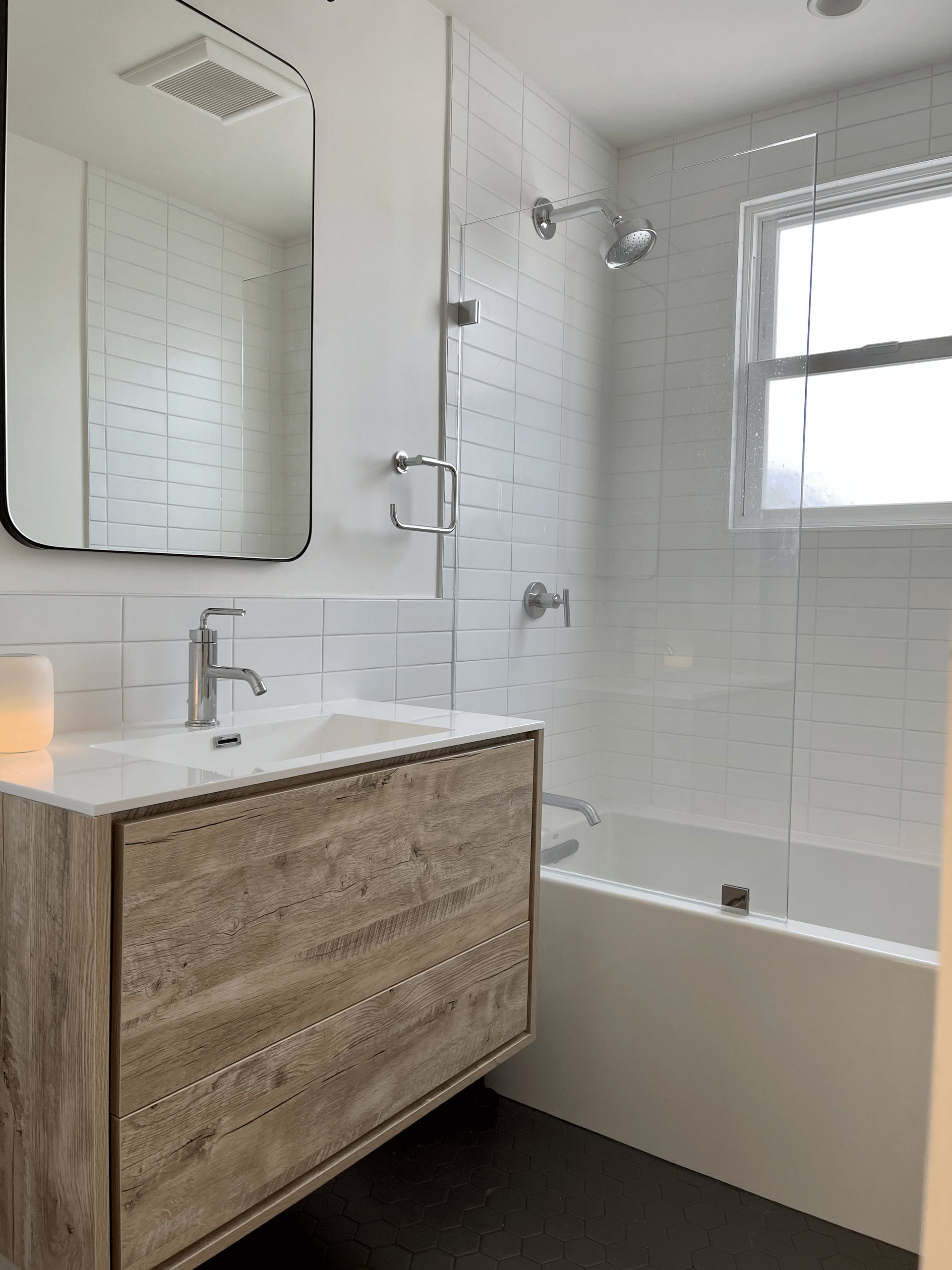 Modern bathroom with white subway tile, wood-look vanity, chrome fixtures, and a small window.