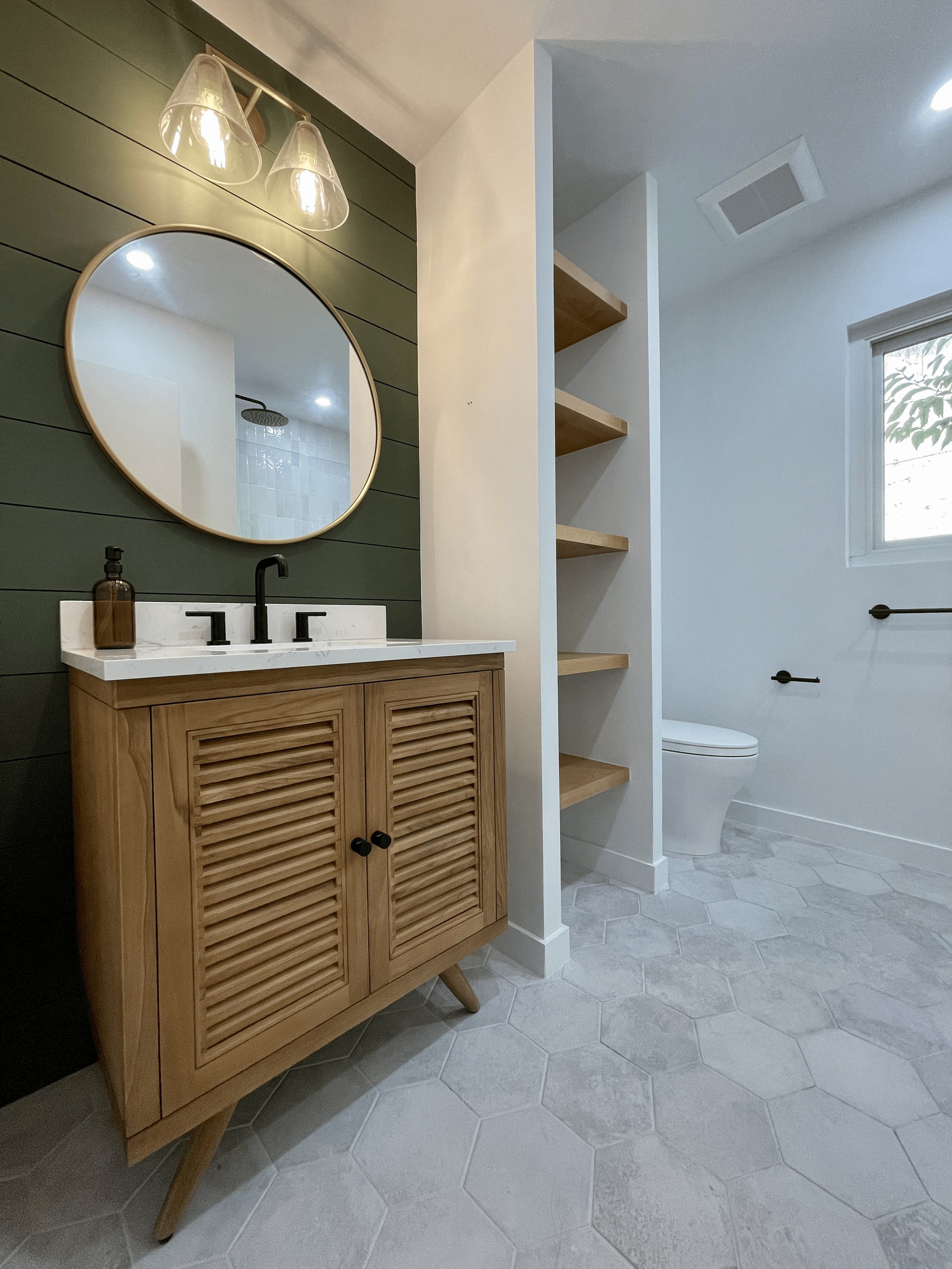 Bathroom with wooden vanity, round mirror, olive green wall, and hexagon tile floor.
