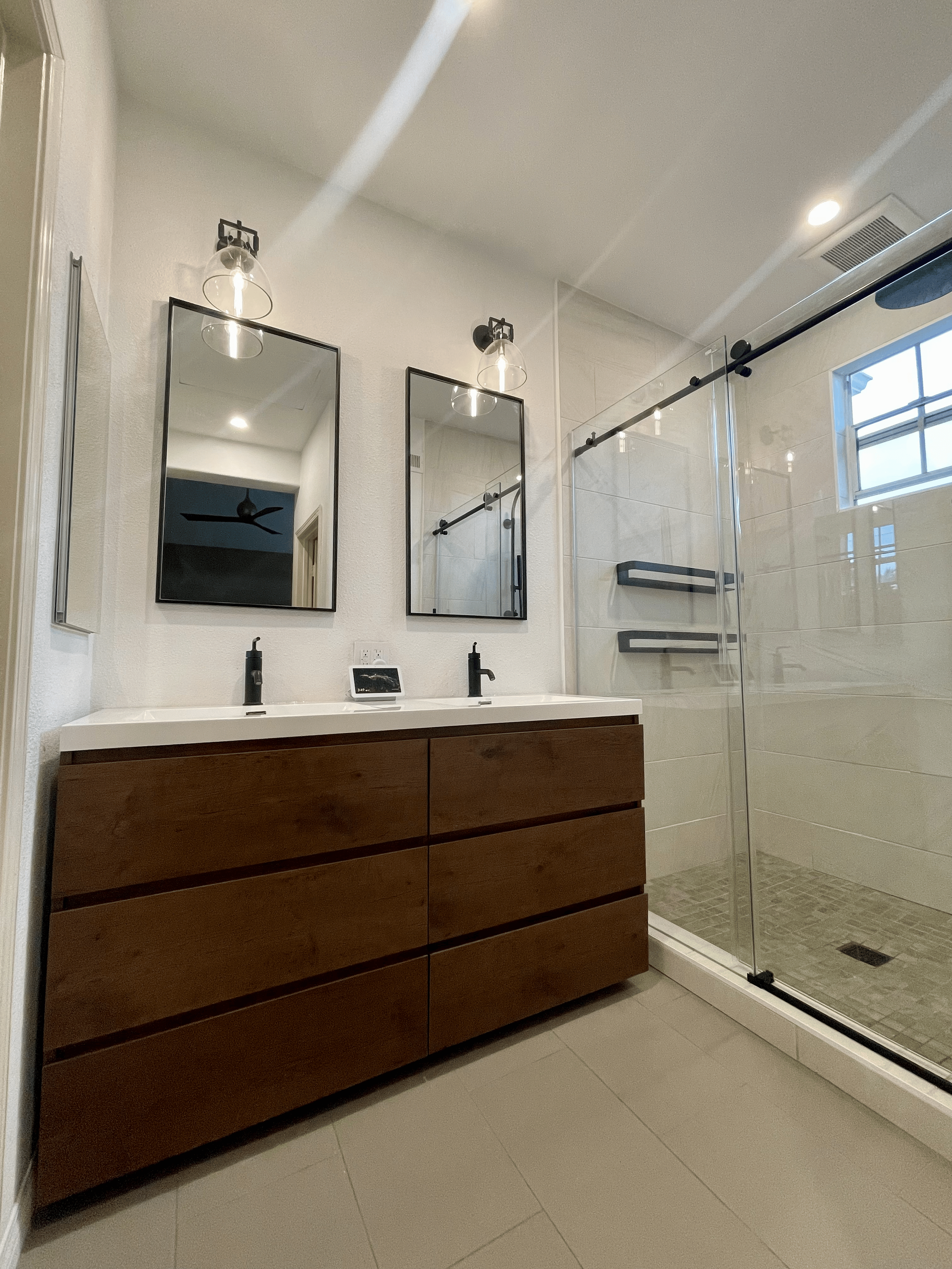 Modern bathroom with a wood vanity, two mirrors, a glass shower, and tile floors.