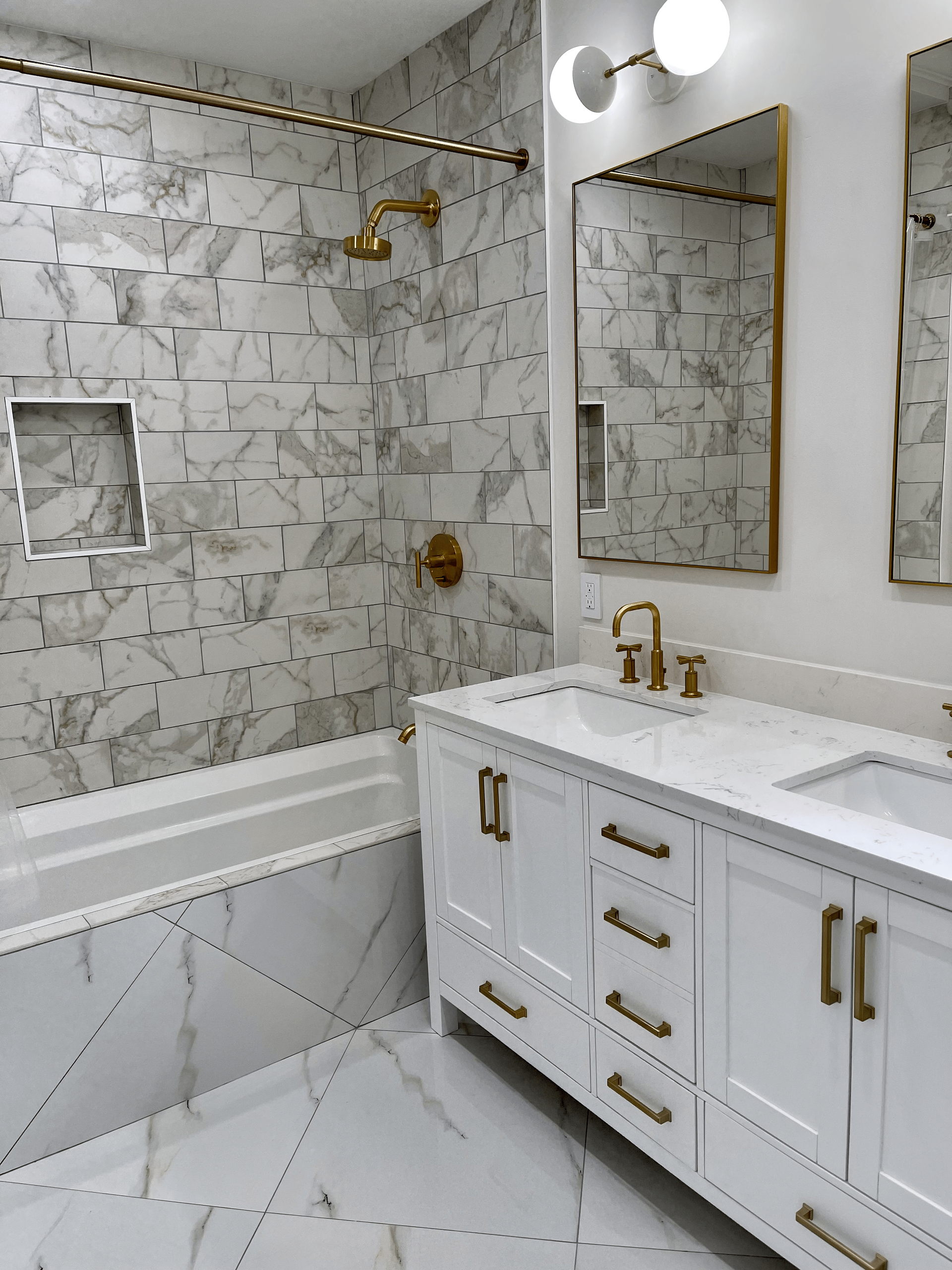 Bathroom with white cabinets, marble tile, gold fixtures, and a bathtub/shower.