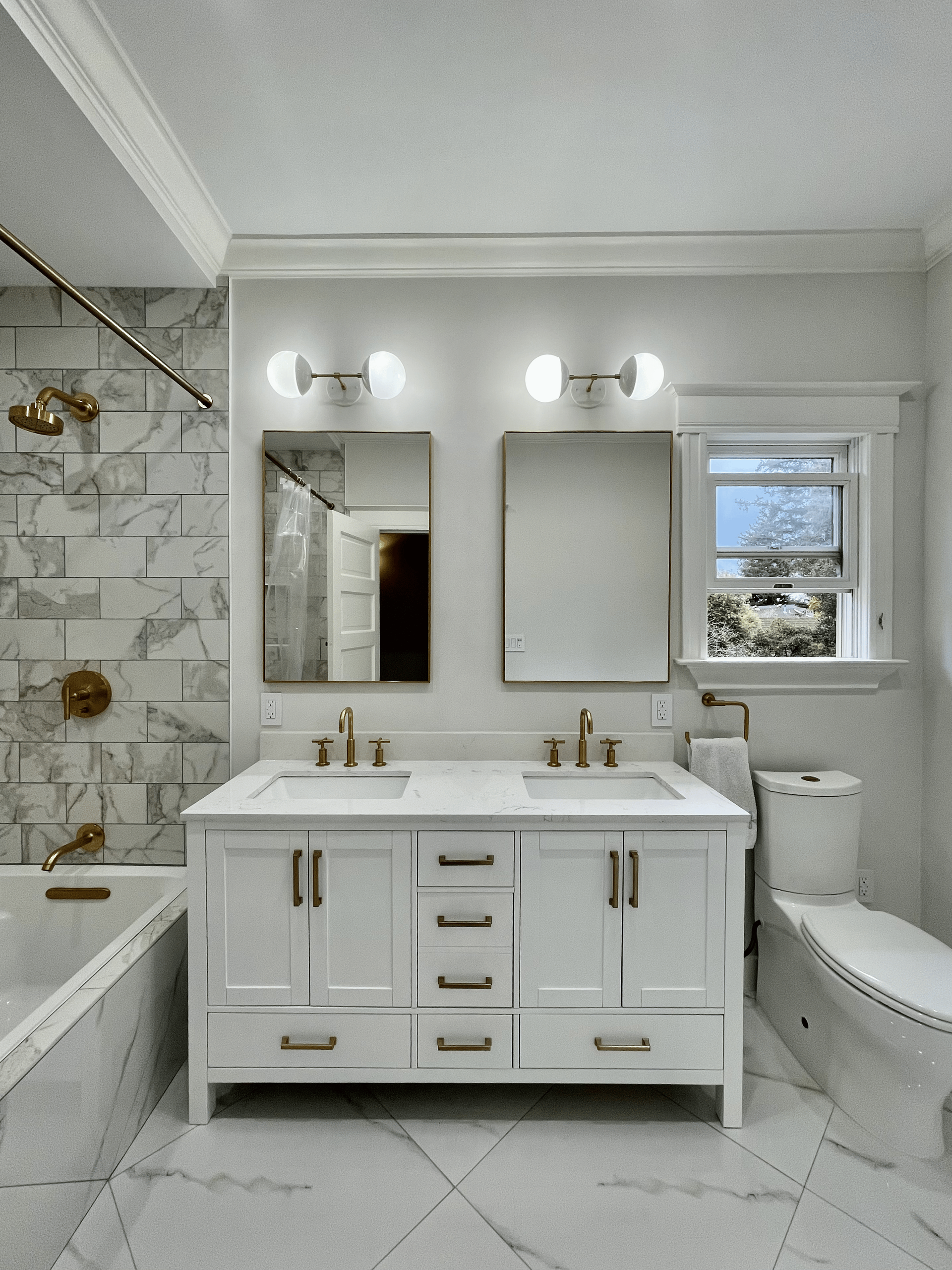 White bathroom with marble tile, a double sink vanity, and a window.