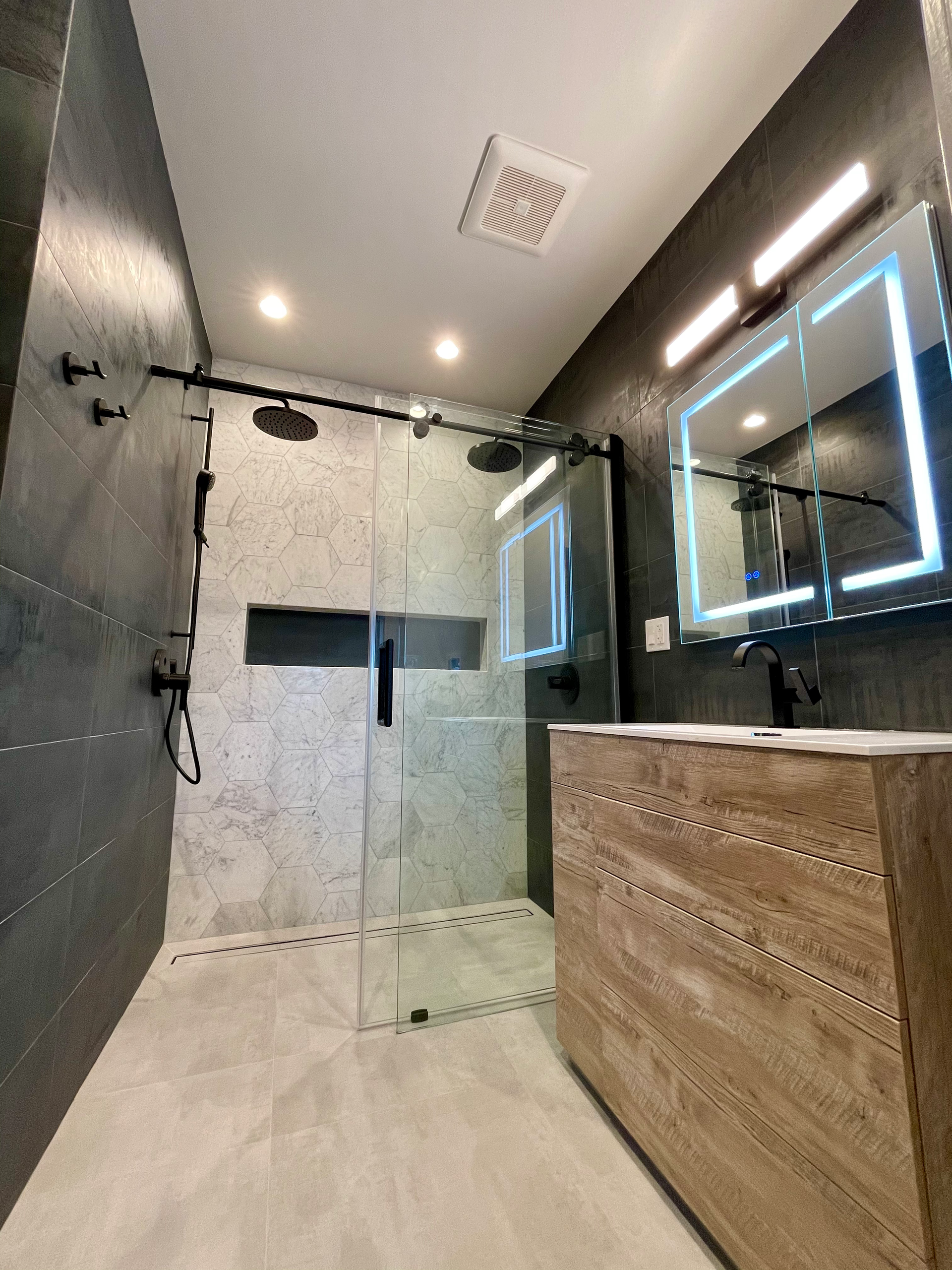 Modern bathroom with a tiled shower and vanity, featuring black fixtures and a wood-look cabinet.