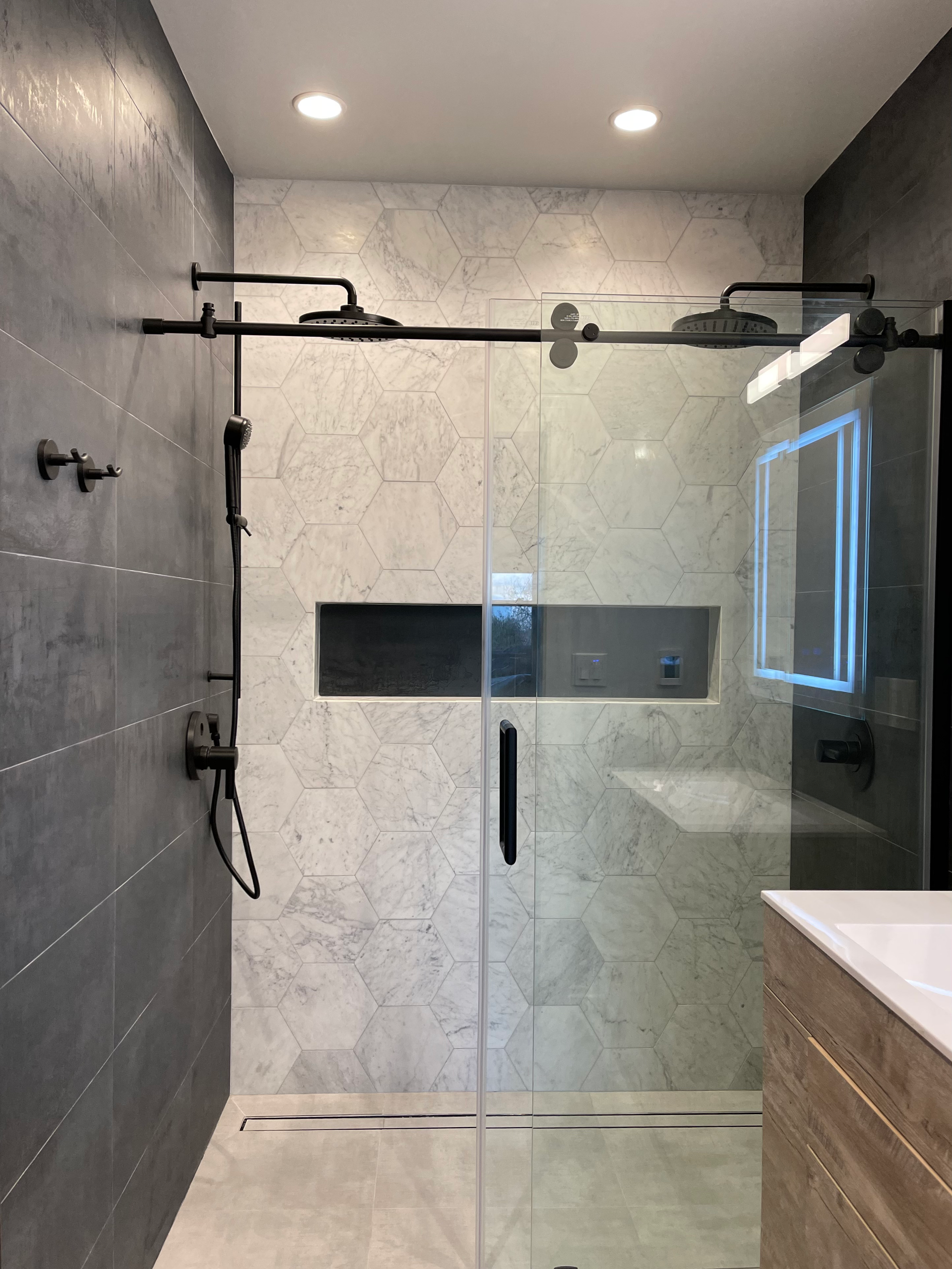 Modern bathroom with a glass shower, dark fixtures, and textured gray and white tile walls.