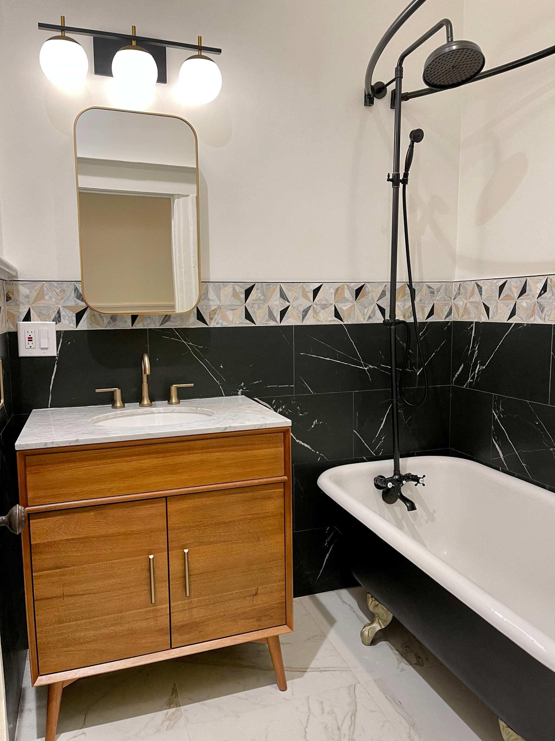 Bathroom with black and white tile, wood vanity, clawfoot tub, and a round mirror.