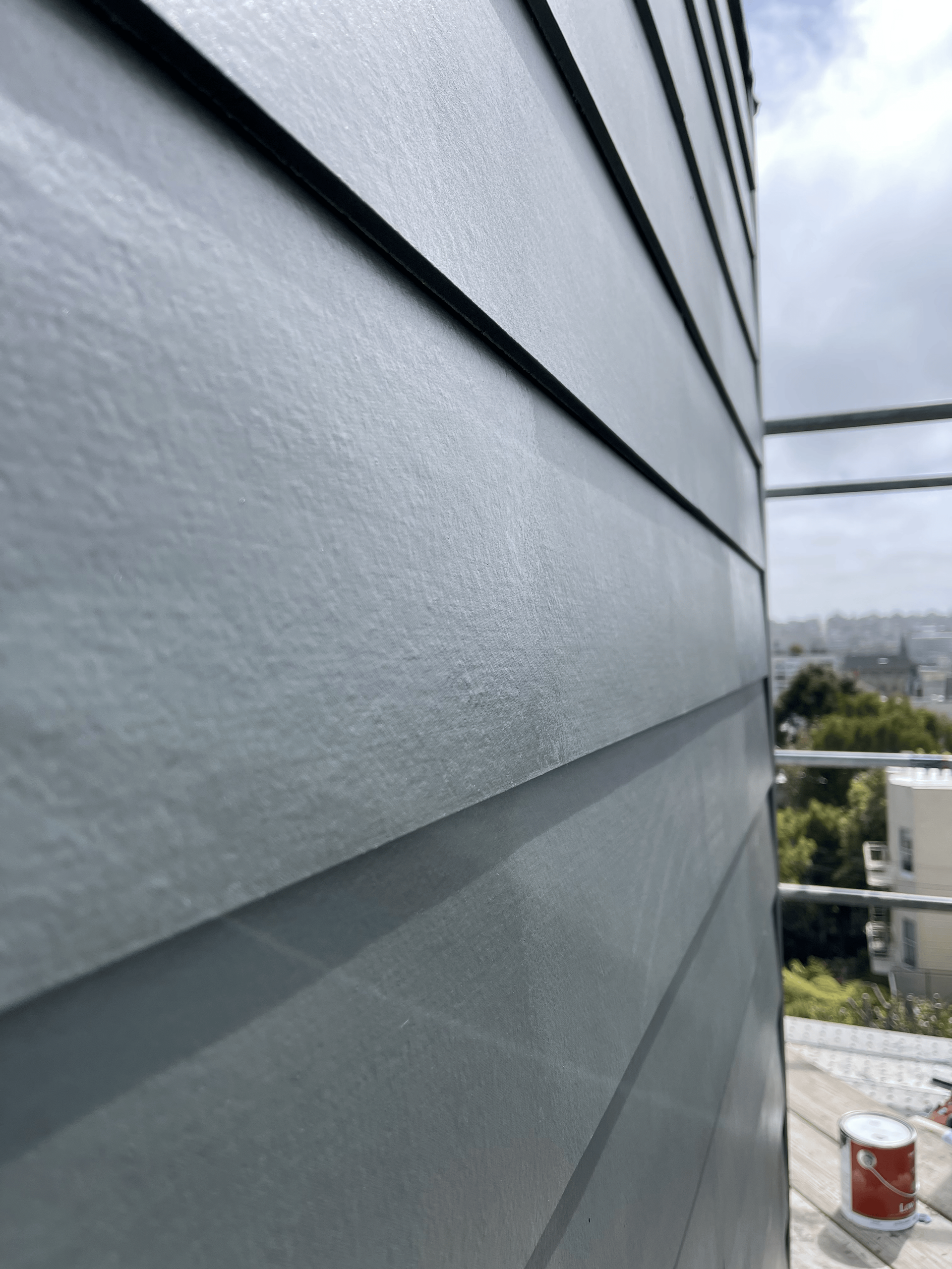 Gray siding on the side of a building, seen from a low angle, with a cityscape in the background.