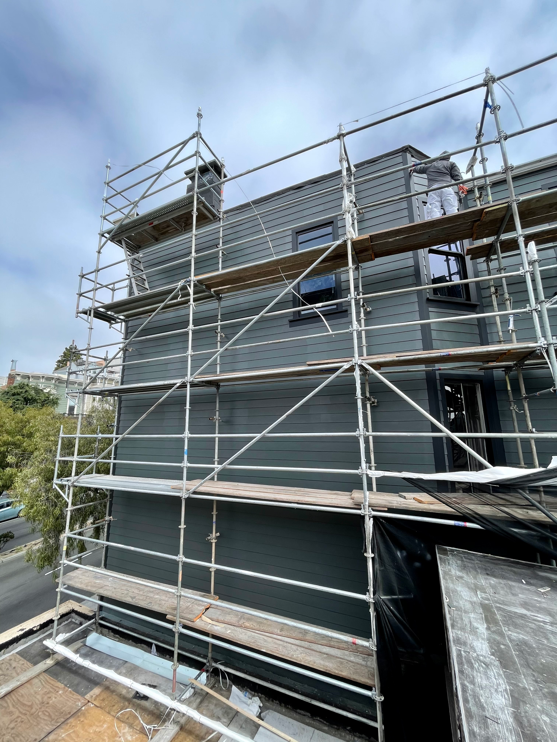 Scaffolding surrounds a gray building under construction. The sky is cloudy.