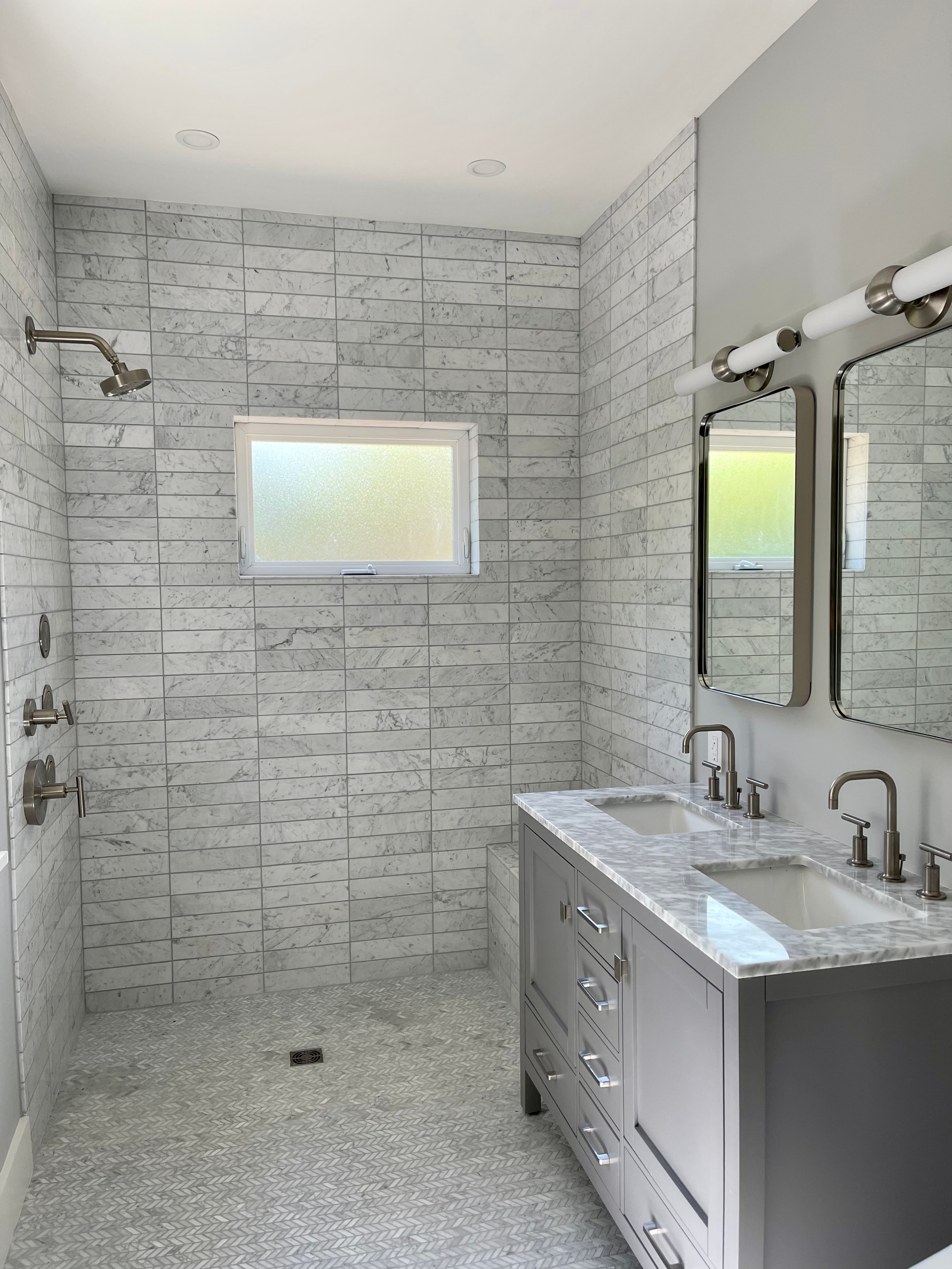 Modern bathroom with gray tiled shower, double vanity, and two mirrors.