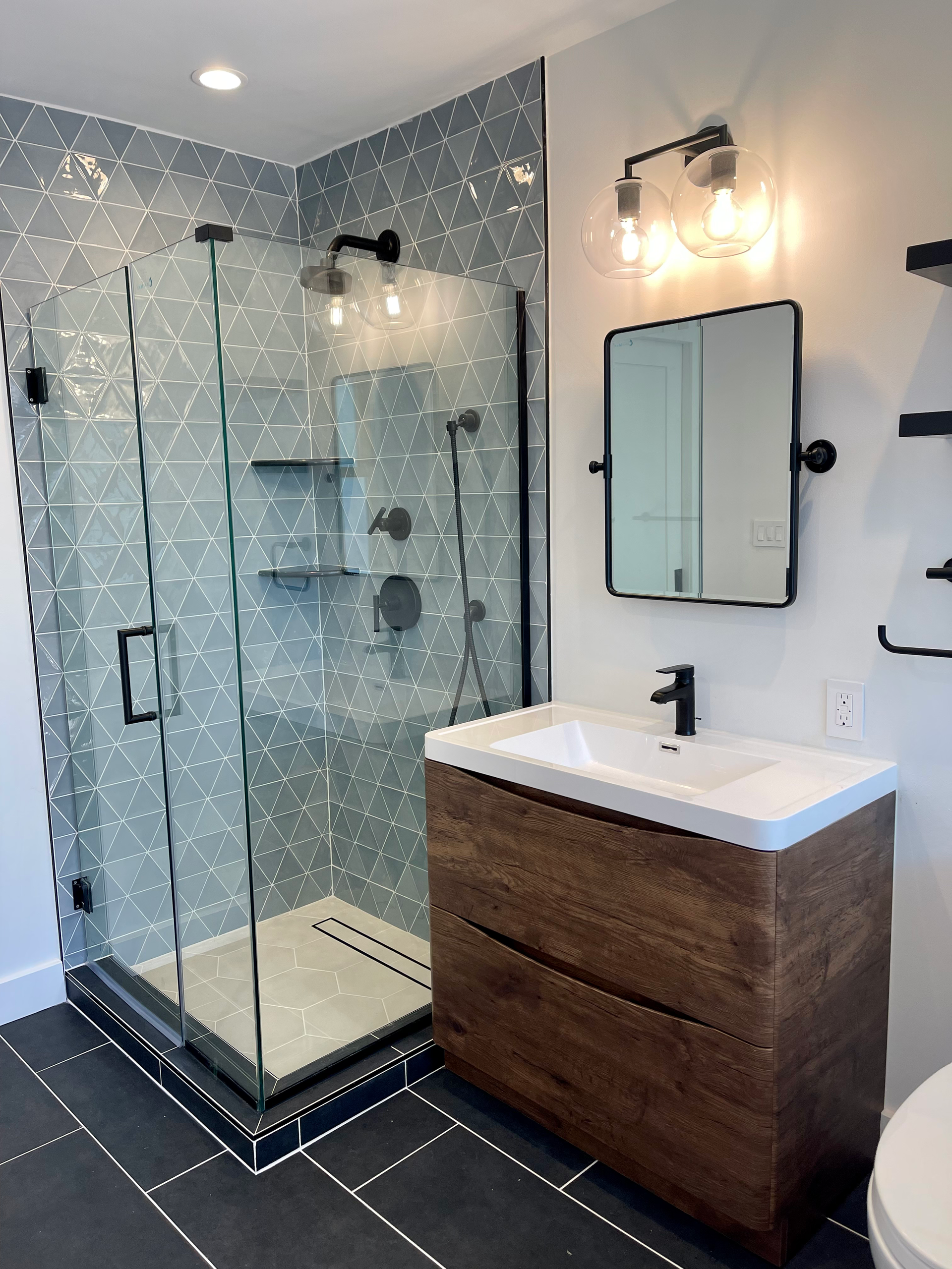 Modern bathroom with glass shower, wood vanity, black accents, and patterned blue tile.