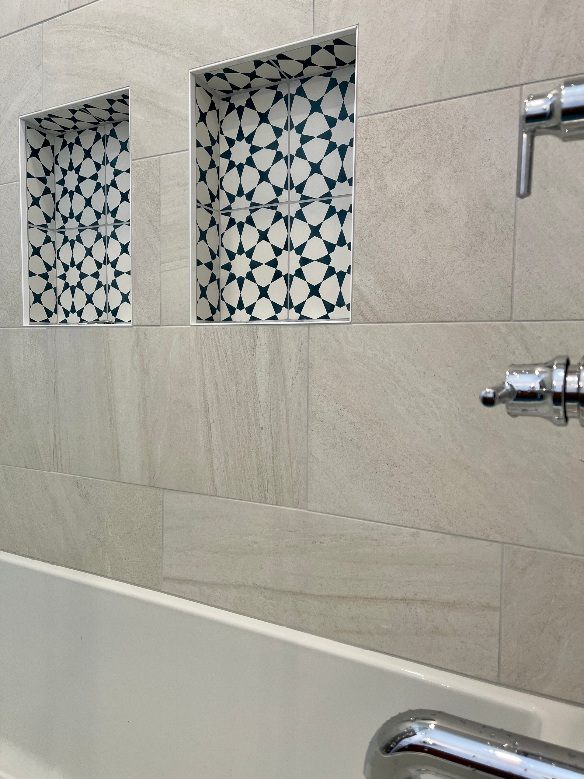 Bathroom with neutral tile and two decorative recessed shelves of patterned blue and white tiles.