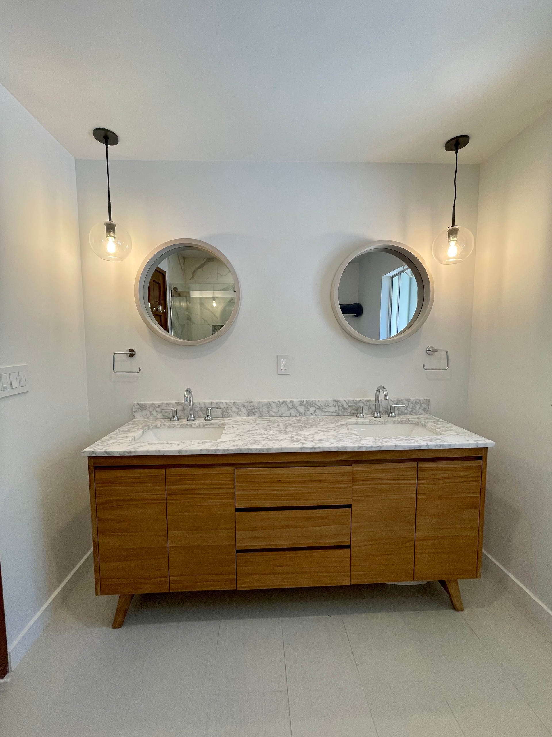 Wooden vanity with granite countertop, round mirrors, and pendant lights in a bathroom.