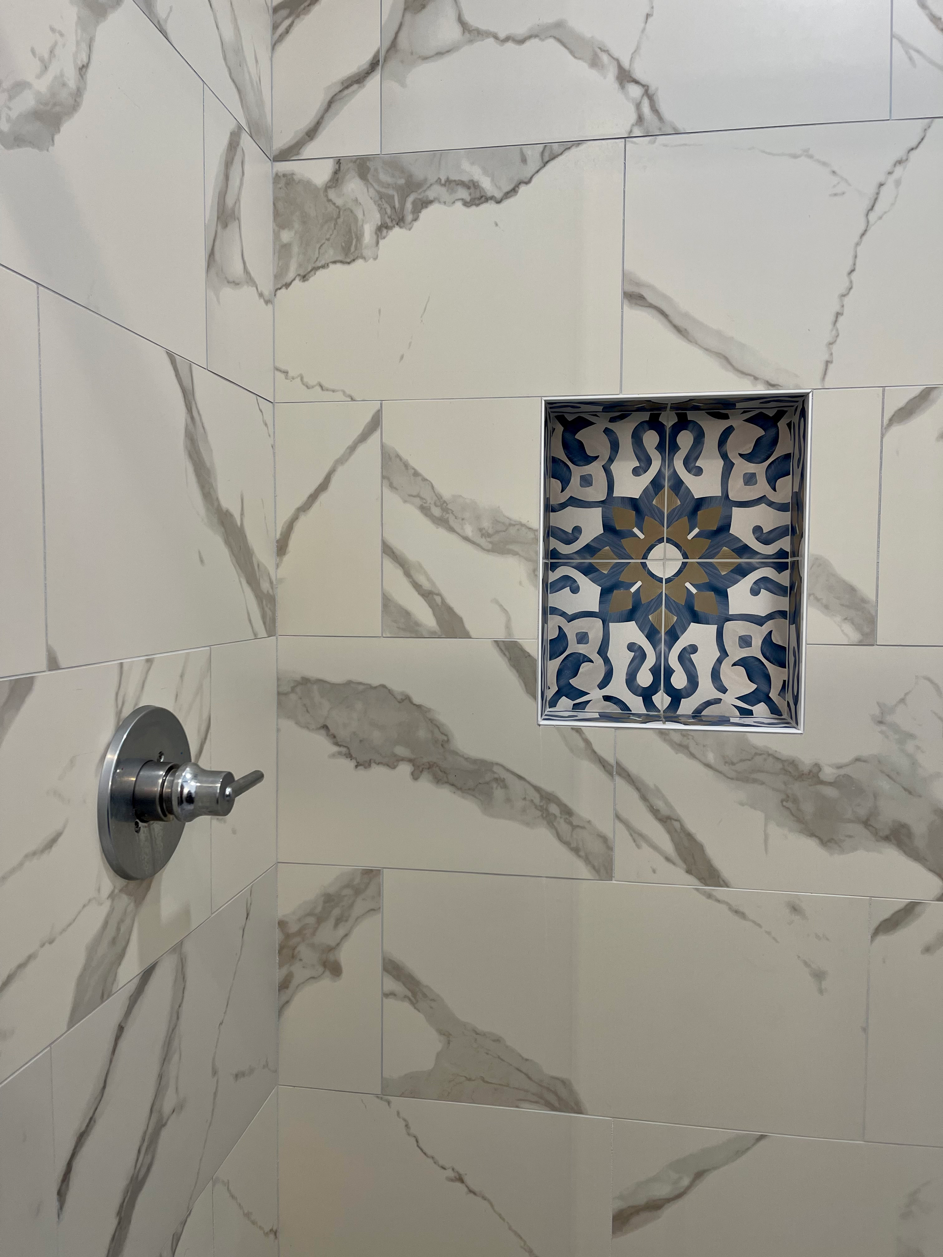 Shower with marble-patterned tiles and a decorative blue and gold tiled niche.