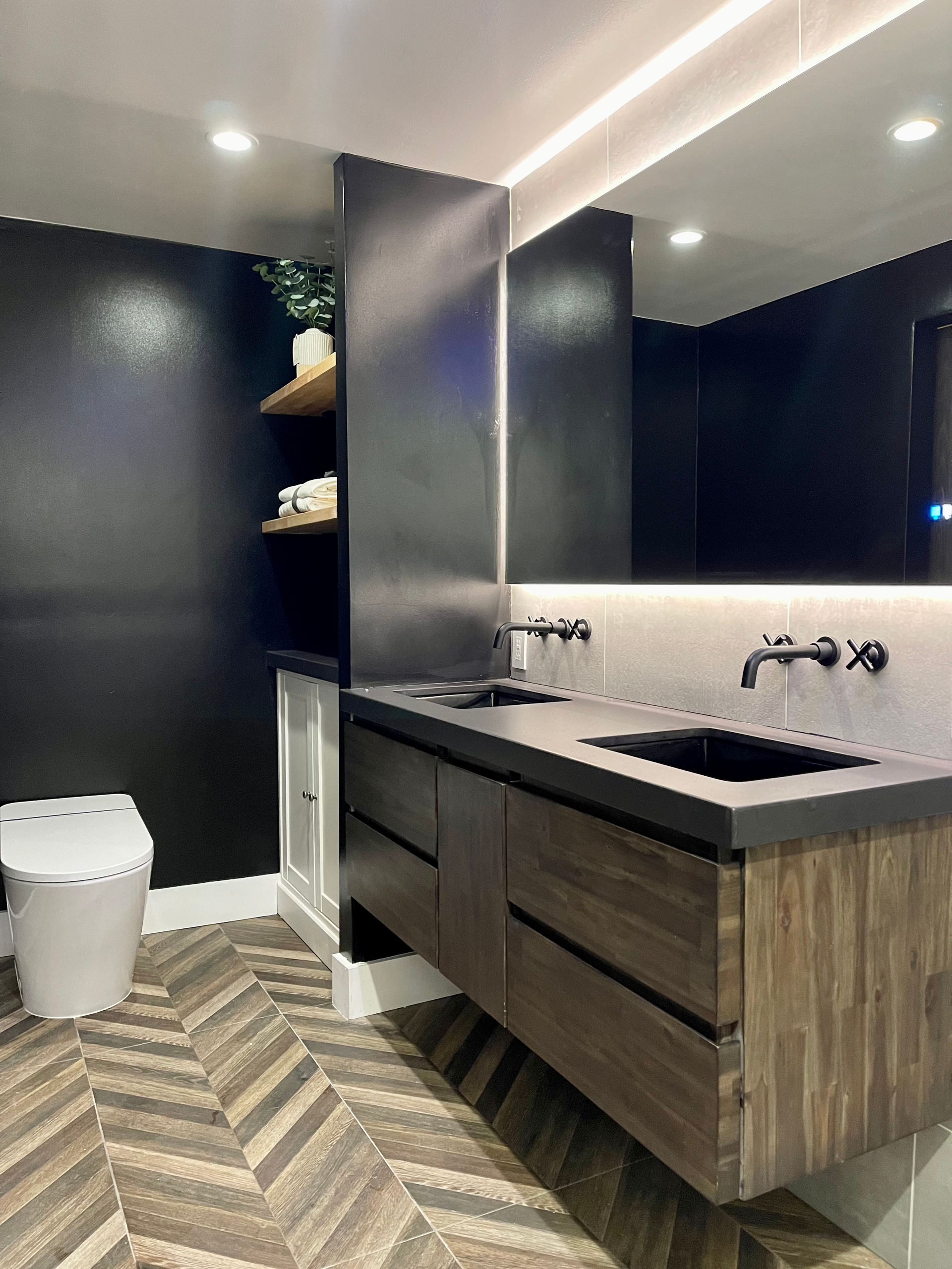 Modern bathroom with black walls, wooden vanity, herringbone floor, and toilet.