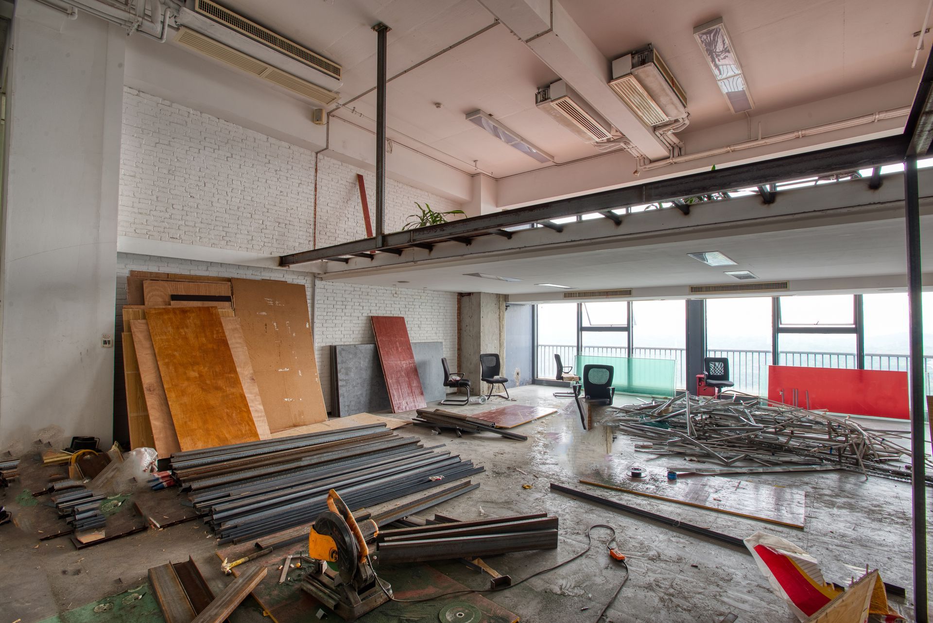 Construction site interior with debris, metal beams, and large boards near an open garage door