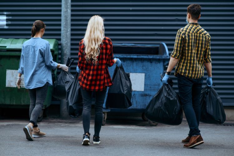 people walking to dumpster to throw garbage bags