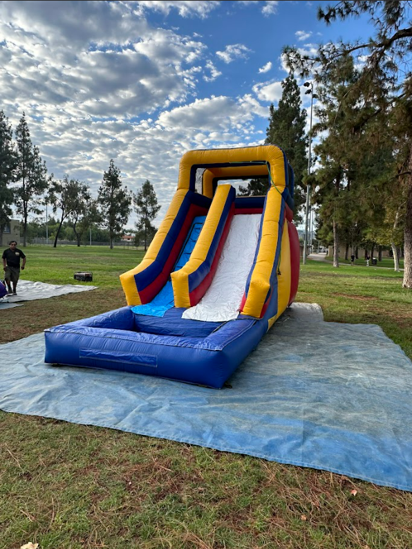 An inflatable water slide is sitting on top of a blue tarp in a park.