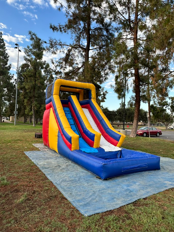 An inflatable water slide is sitting on a tarp in a park.