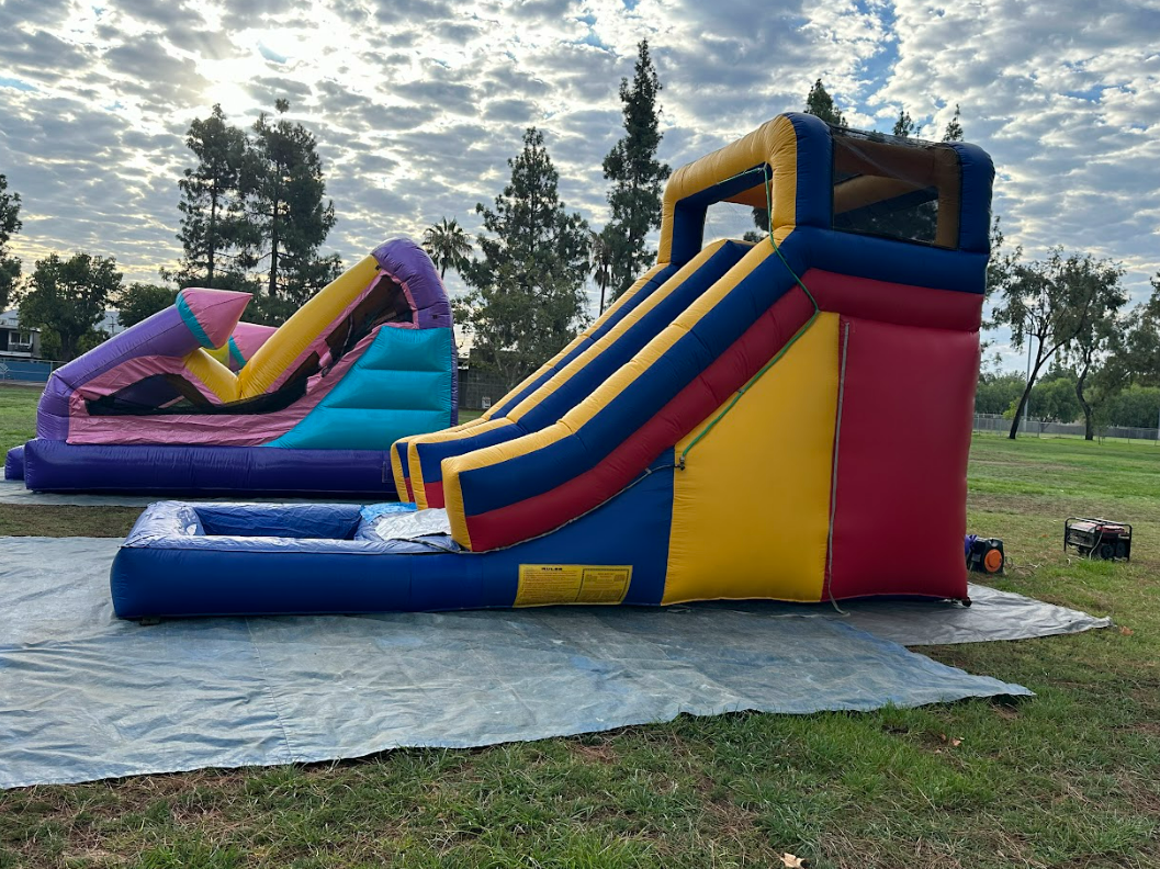 Two inflatable slides are sitting on top of a tarp in a park.