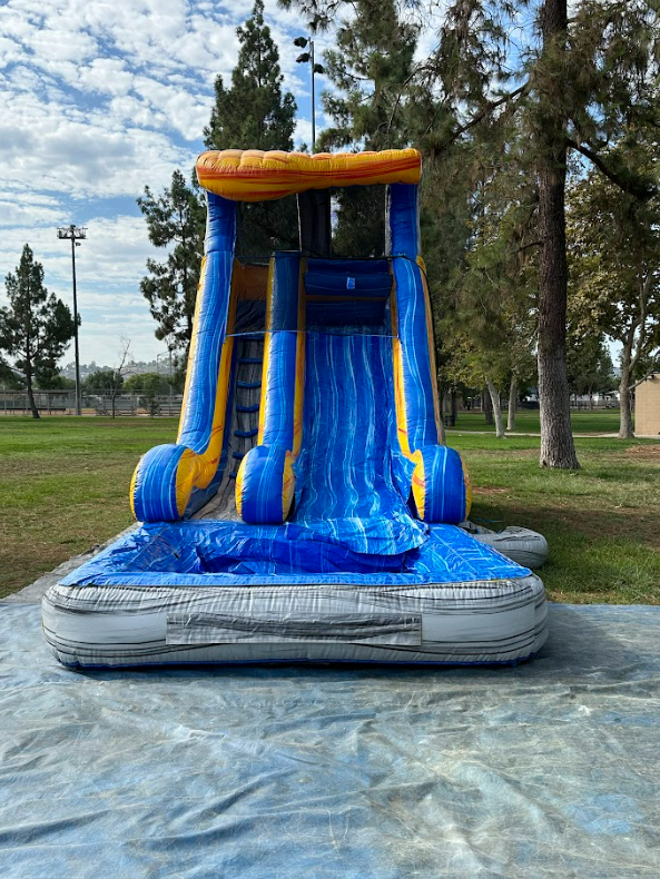 An inflatable water slide is sitting on top of a tarp in a park.