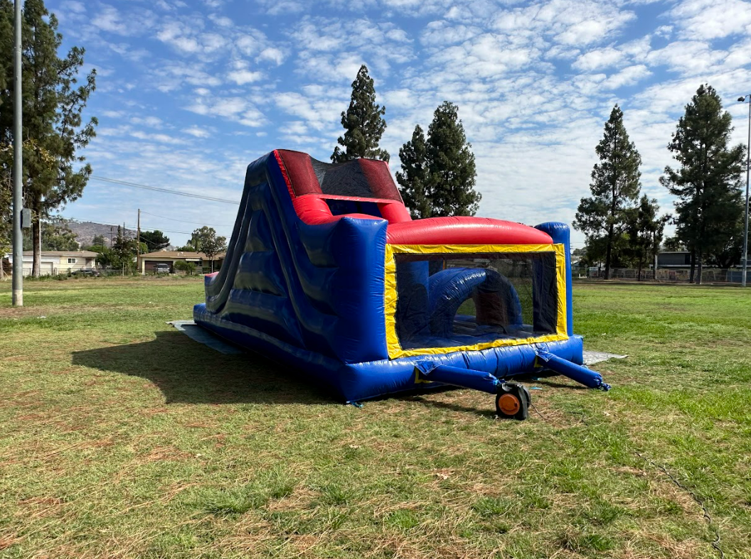 A blue and red bouncy house is sitting in a grassy field.