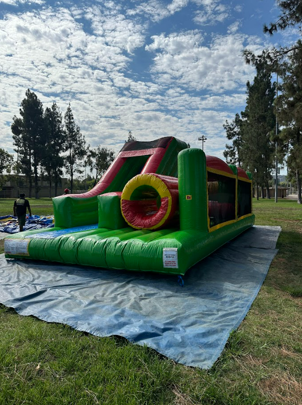 A green and red bouncy house is sitting on top of a tarp in a park.