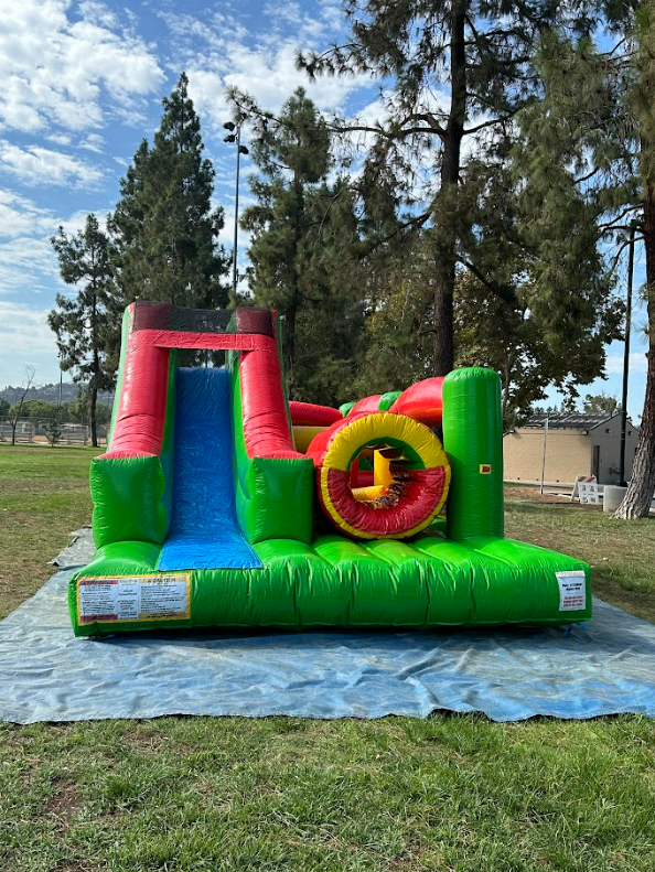 A green and red bouncy house is sitting on top of a tarp in a park.